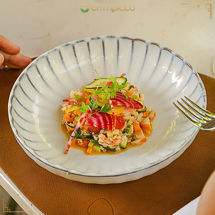 Colorful salad in a decorative bowl with a fork on a wooden surface, featuring the brand 'Olympicco'.